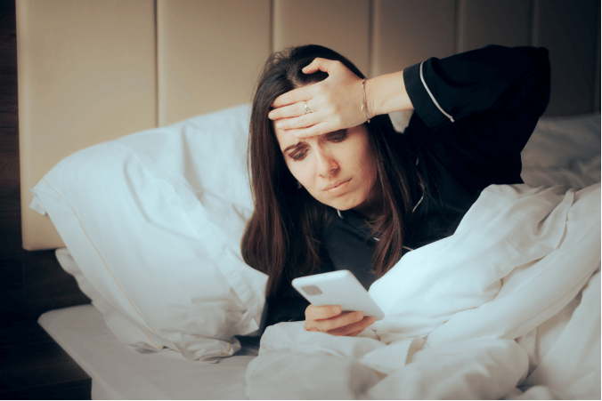 Kranke Frau im Bett mit Smartphone in der Hand