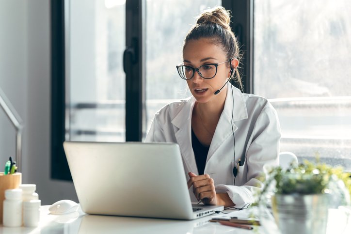 Junge Ärztin mit Headset am Tisch vor ihrem Laptop