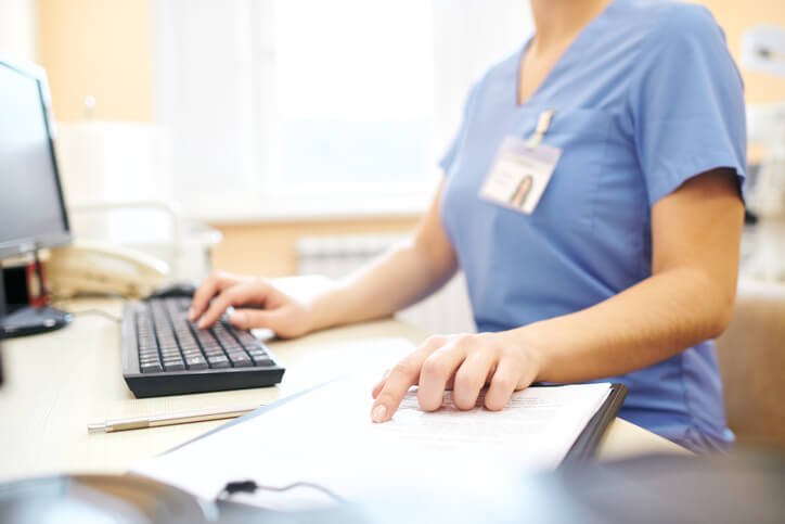 Klinikmitarbeiterin am Schreibtisch mit Computer und Dokumenten